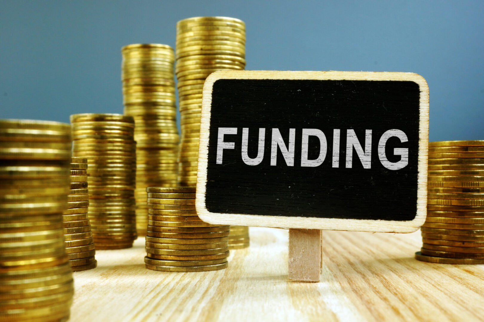 Stacks of gold coins behind a small board labeled 'FUNDING'.