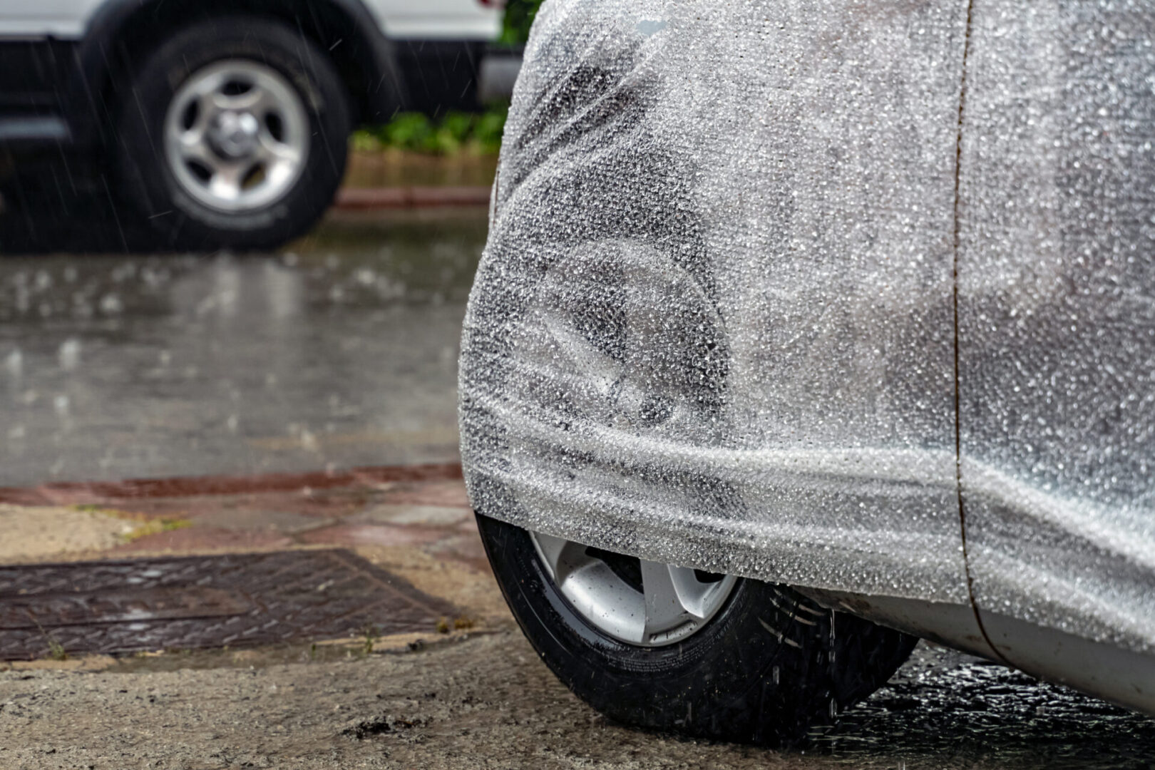 Car covered with a protective plastic sheet on a rainy day.