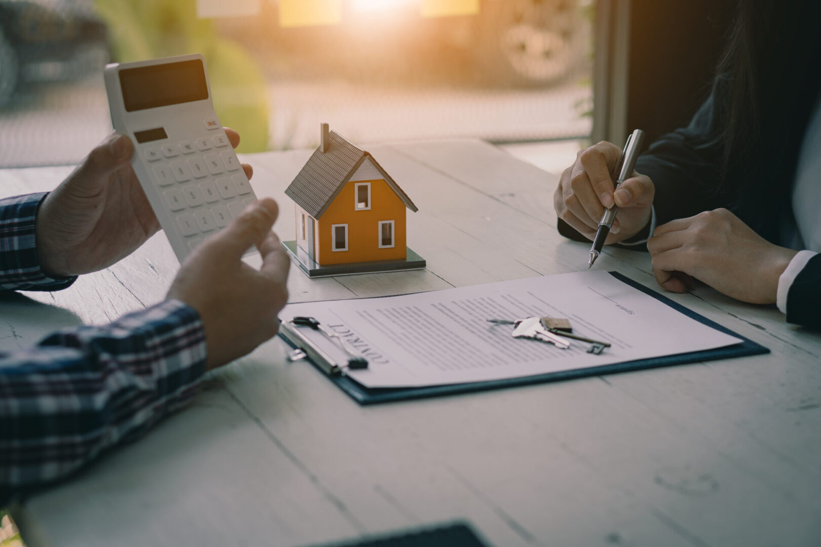People discussing home purchase paperwork with a small house model and keys.