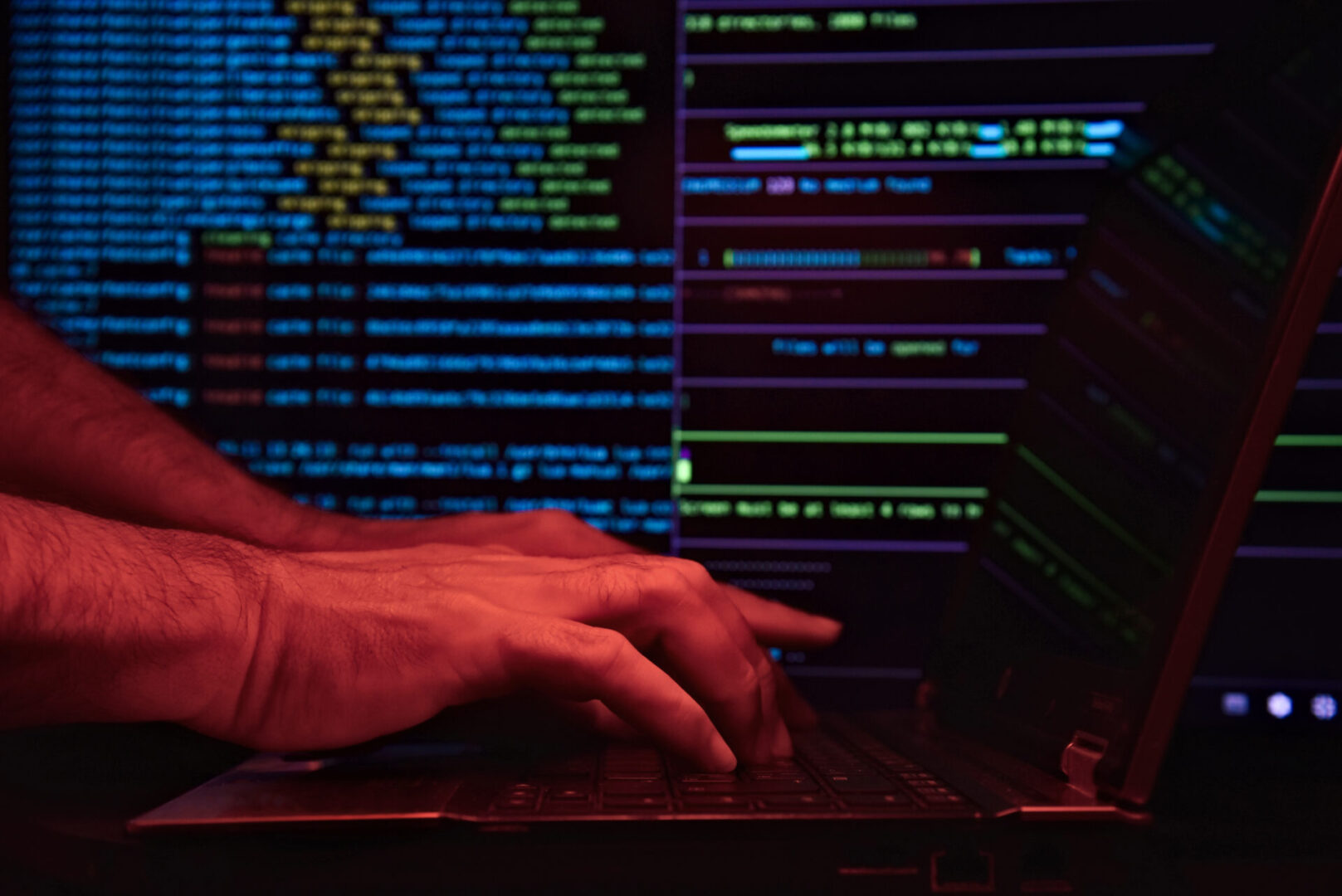 Person typing code on a laptop with multiple coding windows open.