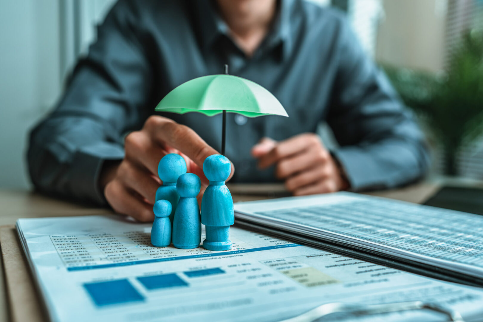 A person shields a small family figurine with a green umbrella symbolizing protection.